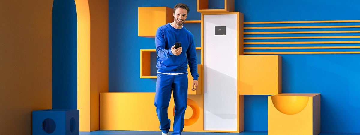 Muž s mobilom v ruke pri vnútornej jednotke tepelného čerpadla SAMSUNG ClimateHub
