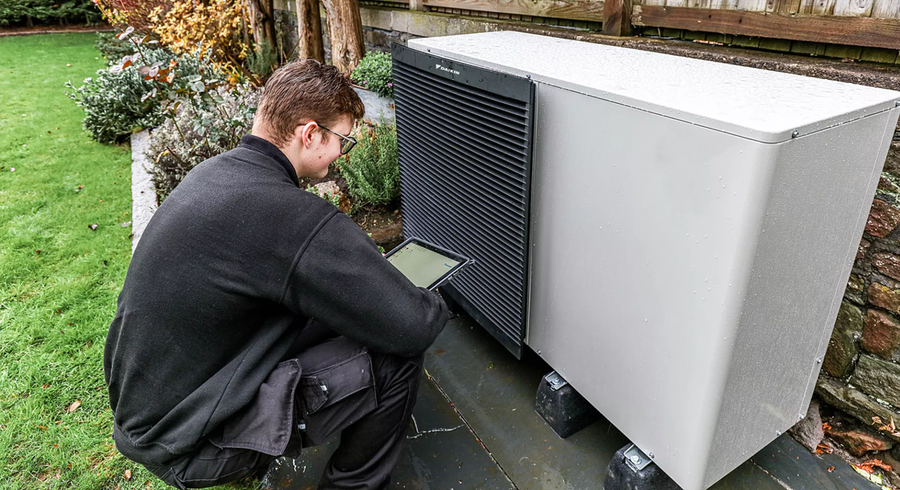 Technik s tabletom kontroluje vonkajšiu jednotku tepelného čerpadla DAIKIN pri kamennom múre v záhrade