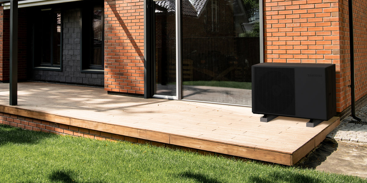 Tepelné čerpadlo SAMSUNG EHS Quint — čierna vonkajšia jednotka na drevenej terase pri tehlovom dome